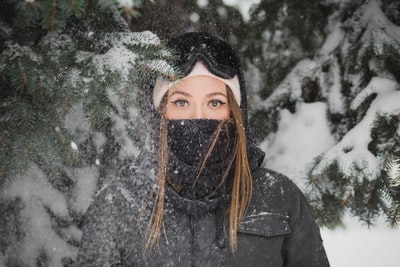 戴着面具的女人站在白雪皑皑的松树旁